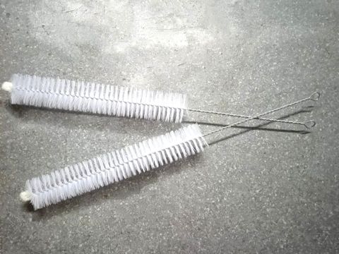 Two white nylon tube brushes with twisted wire handles on a grey surface